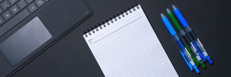 Computer, notitieboekje en drie pennen